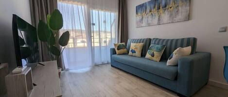 Un salon moderne avec un canapé bleu, un grand tableau et une porte-fenêtre coulissante donnant sur un balcon.