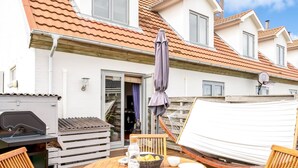 A wooden deck with a round table, chairs, a grill, and a covered seating area.