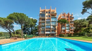 Um hotel moderno com uma piscina grande, rodeado por vegetação exuberante e um céu azul límpido.