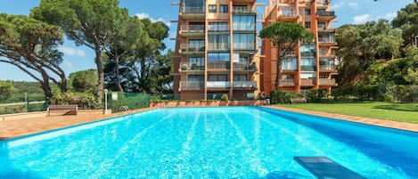 A modern hotel with a large swimming pool, surrounded by lush greenery and a clear blue sky.