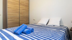 Quarto com cama, duas almofadas, colcha azul e branca listrada e um guarda-roupa de madeira.