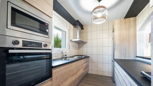 Une cuisine moderne dotée d’un four encastré, d’un évier en acier inoxydable, de meubles de rangement en bois et d’un plan de travail noir.