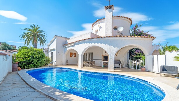 Une piscine à bord incurvé, un bâtiment blanc orné d’arches et un palmier.