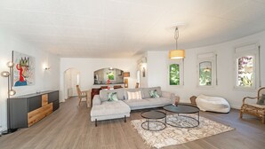 Un salon spacieux avec un canapé gris, deux petites tables rondes et un coin repas comprenant une table et des chaises en bois.