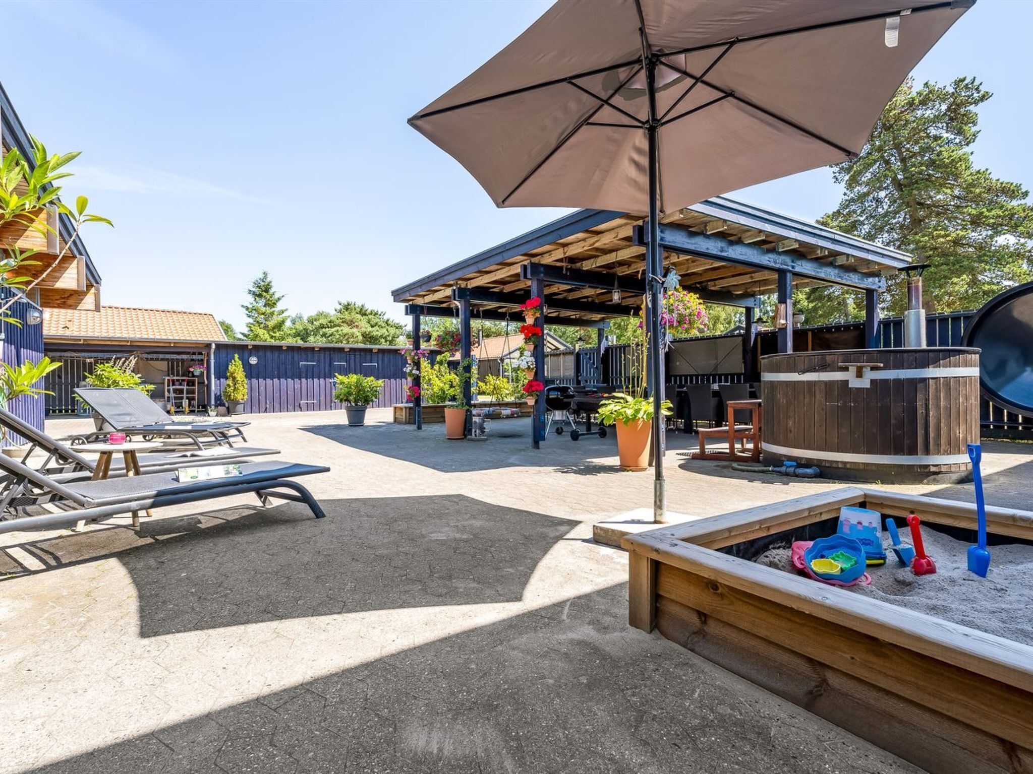 A covered outdoor area with a barbecue grill, lounge chairs, and a sandbox.