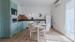 A modern kitchen with teal cabinets, a dining table with chairs, and a large window. - Pine's Mansion by Interhome (Le Barcarès)
