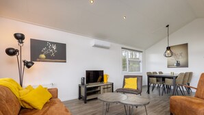 A living room with a sofa, coffee table, TV, and dining area with chairs. - Scenic Retreat by the Lake (Hoge Hexel)