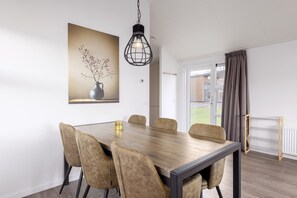 Un coin repas avec une table et des chaises en bois, un luminaire suspendu, un tableau au mur et une vue par la fenêtre.