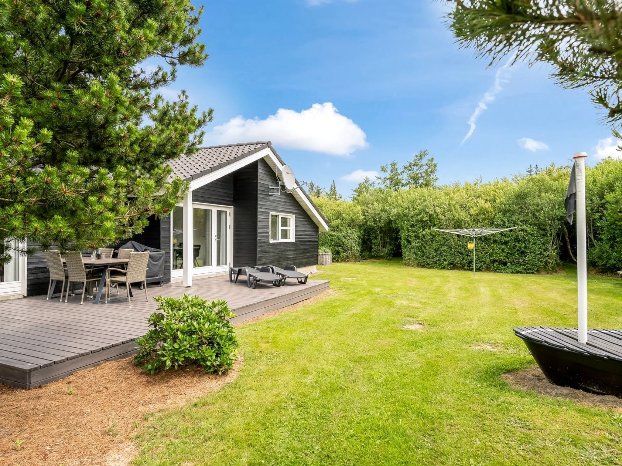 A modern house with a deck, outdoor seating, and a well-maintained lawn.