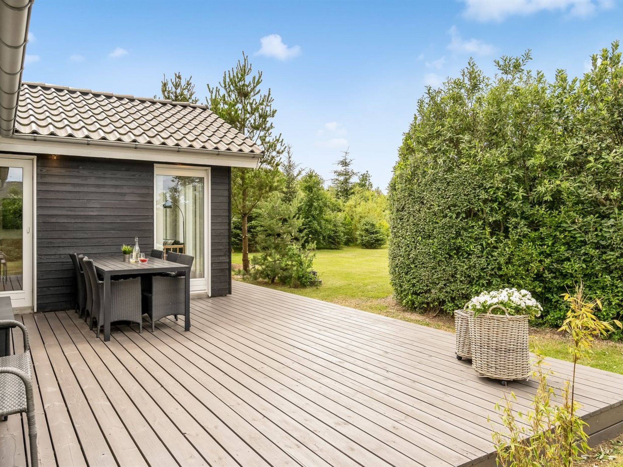 A modern house with a deck, a dining area with outdoor furniture, and a well-maintained garden.