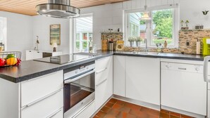 A modern kitchen with white cabinets, a stainless steel range hood, a built-in oven, and a large window providing natural light.