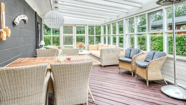 A sunlit patio with wicker furniture, a dining table, and a large fan.