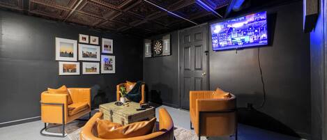 A modern living room with a high ceiling, framed pictures, a dartboard, and a television.