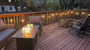 Eine Holzterrasse mit Feuerstelle, Sitzgelegenheiten und Lichterketten.