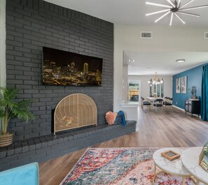 A modern living room with a fireplace, a cityscape painting, and a dining area with a chandelier. - mins to stadium -Speakeasy-game room-Poker and pool table-heated cowboy pool- (Grand Prairie)