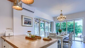 A modern kitchen with a wooden island, a dining area with a chandelier, and large windows offering a view of the outdoors. - Ardiletta by Interhome (Poreč/Baderna)