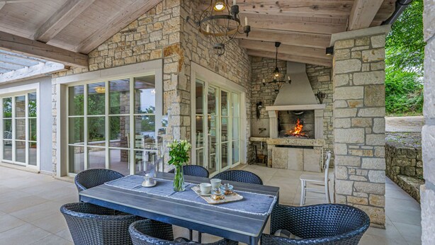 An outdoor patio with stone walls, a fireplace, wicker furniture, and a dining table. - Ardiletta by Interhome (Poreč/Baderna)