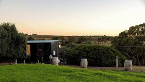 A rural setting with a small building, barrels, and a grassy field. - Scrub Tiny House by Tiny Away (McLaren Vale)
