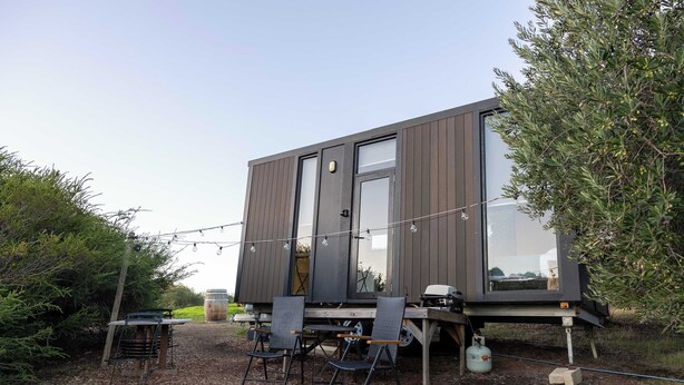 A modern, compact mobile home with large windows, a patio with outdoor seating, and a barbecue grill. - Scrub Tiny House by Tiny Away (McLaren Vale)