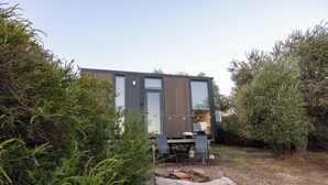 A modern cabin with a deck, surrounded by dense vegetation. - Scrub Tiny House by Tiny Away (McLaren Vale)
