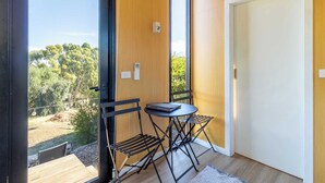 A room with a large window, a small table with chairs, a door, and a wall-mounted light fixture. - Scrub Tiny House by Tiny Away (McLaren Vale)