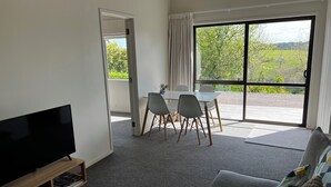 A living room with a flat-screen TV, a grey sofa, and a dining area with a table and chairs. - Tranquil retreat in close proximity to Auckland (Ararimu)