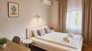 Un dormitorio con cama, mesita de noche, silla y escritorio con una planta.