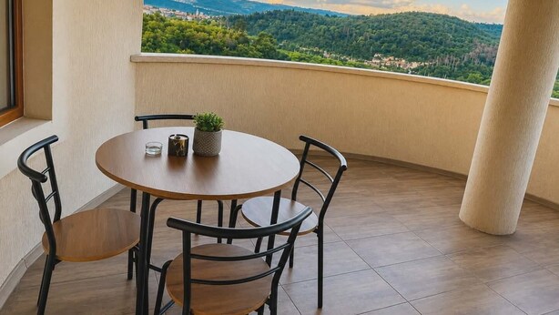 Un balcón con una mesa redonda y sillas, una planta pequeña en maceta, y vistas de un paisaje montañoso.