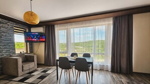 Una habitación moderna con una pared de acento de piedra, un televisor de pantalla plana, una mesa de comedor con sillas y un ventanal con cortinas.