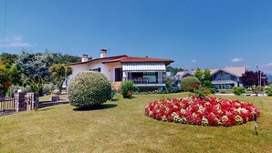 A two-story house with a red-tiled roof, surrounded by well-maintained gardens and a clear blue sky.