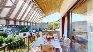 A balcony with a table set for dining, overlooking a parking area and greenery.