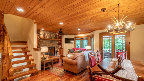 A wooden interior with a staircase, a fireplace, a sofa, and a dining table. - Mountain Retreat - walk to Main Street (Lake Placid)