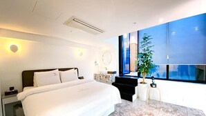 A modern hotel room with a large bed, a small desk, a potted plant, and a large window offering a view of the city. - Garden Pool Villa (Seoul)