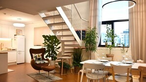 A modern kitchen with white cabinets, a dining area with white chairs and a table, and a staircase with a white railing. - Garden Pool Villa (Seoul)