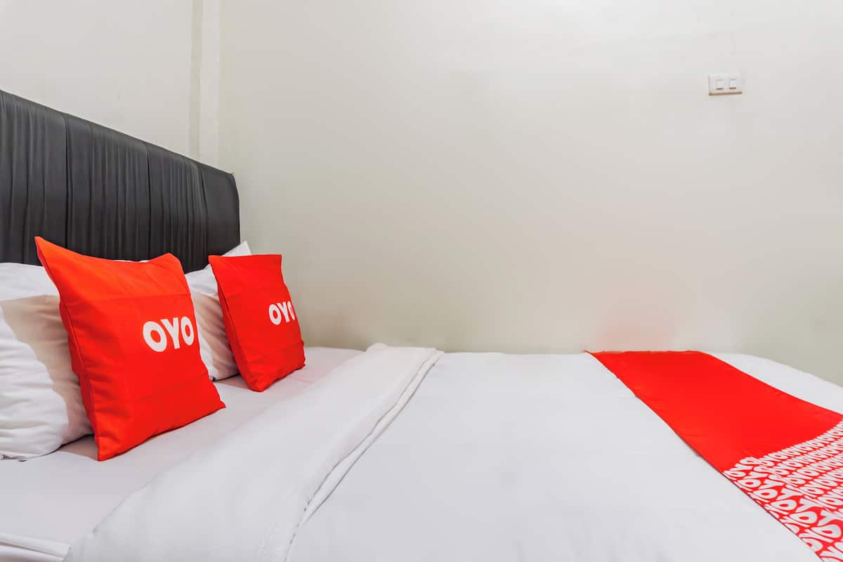 Une chambre d’hôtel avec un lit, du linge de lit blanc et des oreillers rouges sur lesquels est inscrit le mot « OYO ».