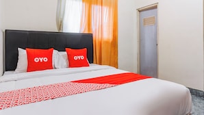 A hotel room with a bed, two red pillows with the word "OYO" on them, a white bedspread, and an orange curtain. - Hotel O The Roy Suite Guest House (Bandar Lampung)