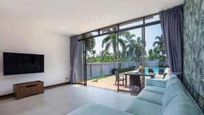 A modern living room with a large TV, a sofa, and a view of an outdoor pool area. - Modern 3BR Pool Access Villa Argent 6 (Thep Krasattri)