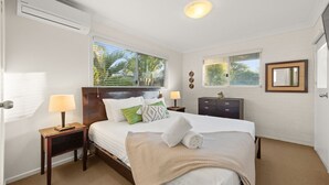 Une chambre à coucher avec un lit, deux tables de chevet avec des lampes, une commode, une fenêtre avec des stores et un miroir sur le mur.