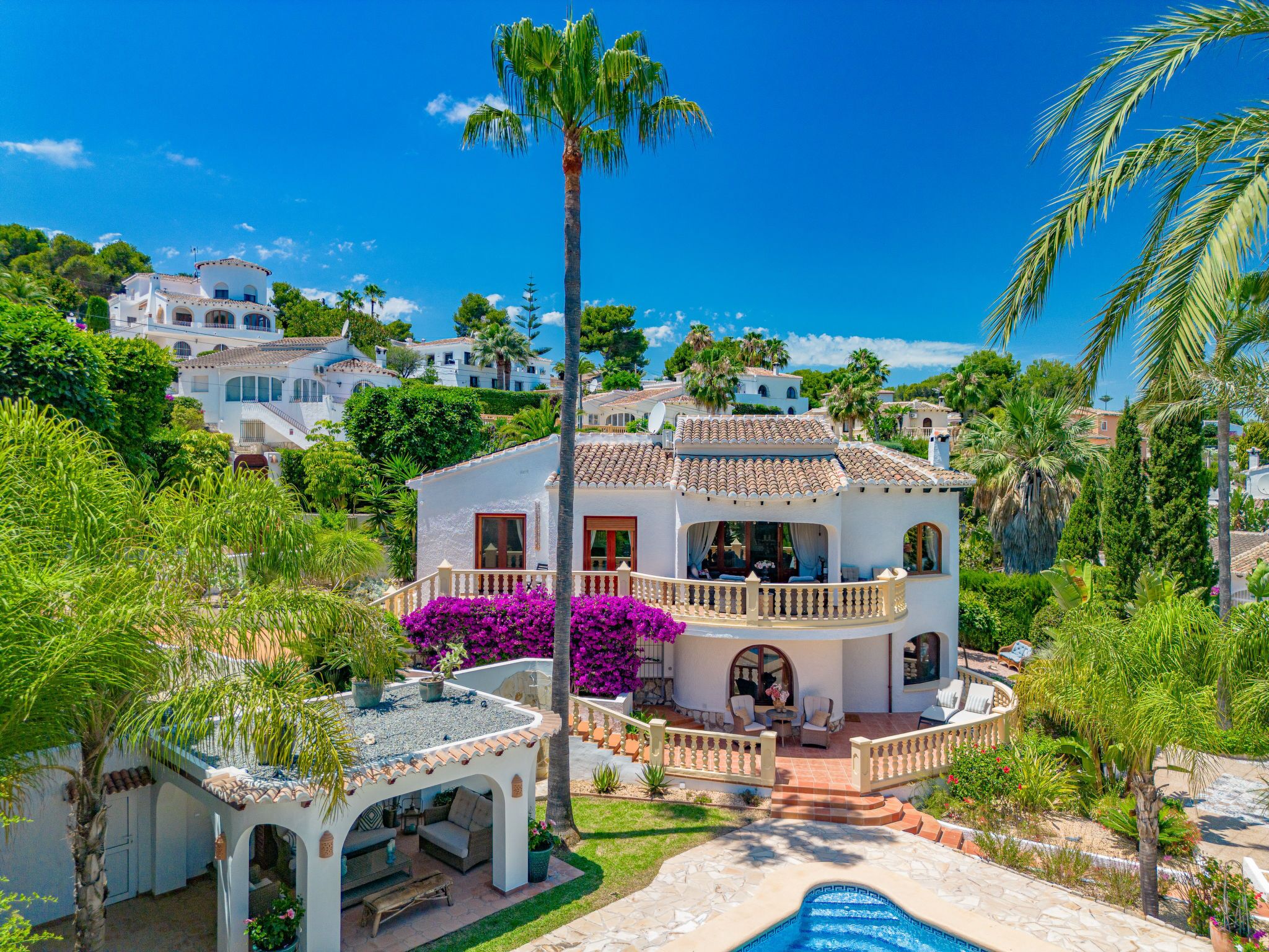A large, two-story house with a balcony, surrounded by lush greenery and a swimming pool.