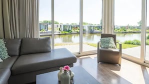 Ein modernes Wohnzimmer mit großem Fenster, einer Couch, einem Sessel und einem kleinen Tisch mit einer Vase.