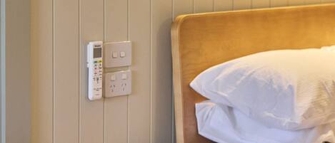Una mesita de noche de madera con tapa redonda, ubicada al lado de una cama con ropa de cama blanca.