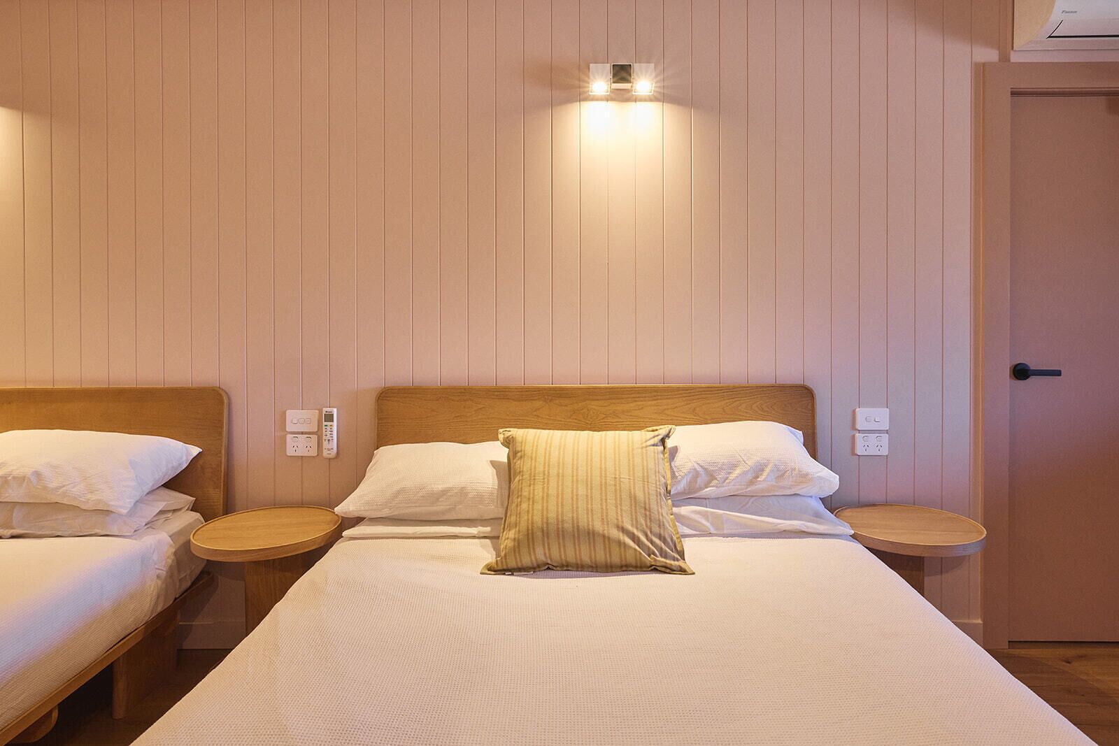 A hotel room with two beds, wooden headboards, bedside tables, and a wall-mounted light fixture.