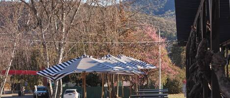 A park with picnic tables, a striped canopy, and a building with a sloped roof.