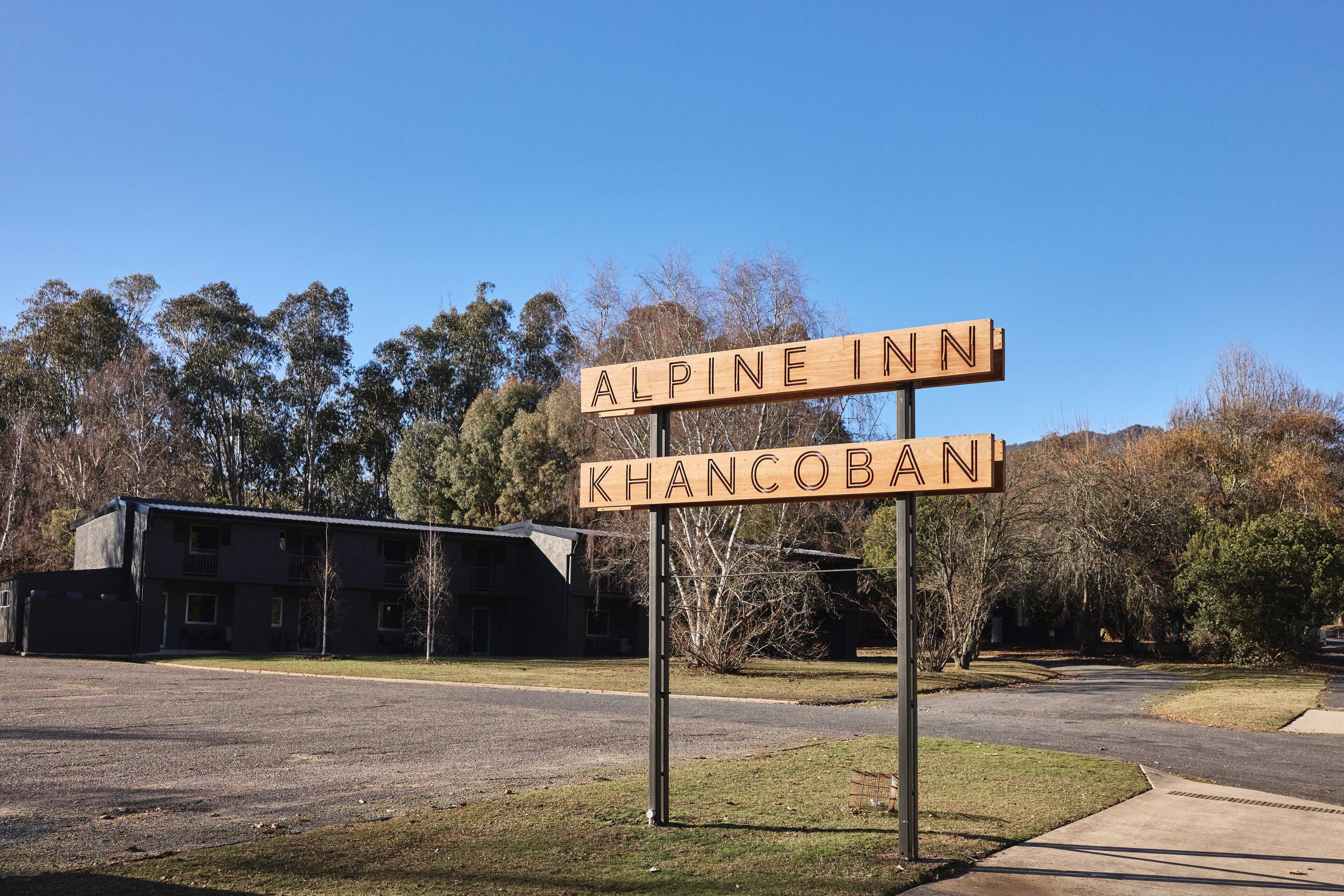 A sign for 'Alpine Inn' and 'Khancoban' in a rural setting with a building in the background.