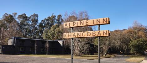 A sign for 'Alpine Inn' and 'Khancoban' in a rural setting with a building in the background.