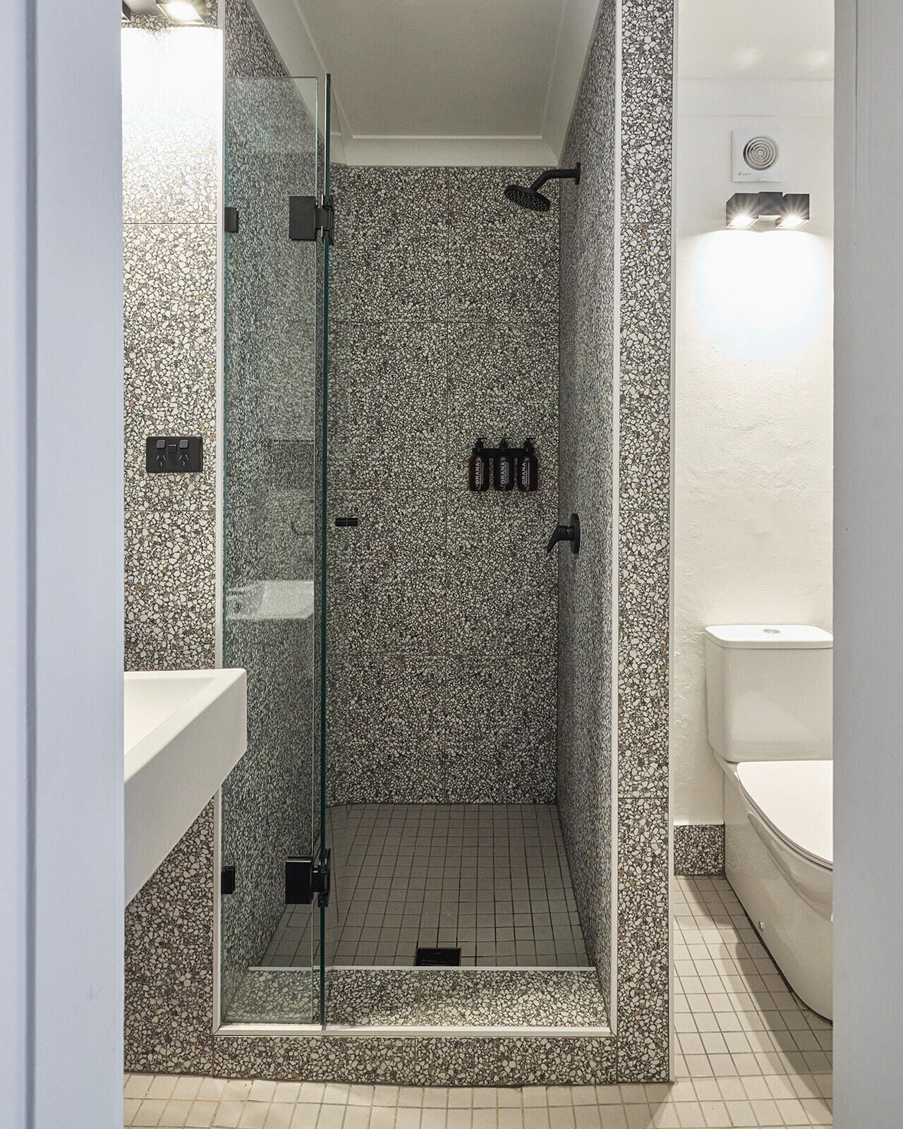 A modern bathroom with a glass-enclosed shower, pebble-patterned walls, and a white toilet.