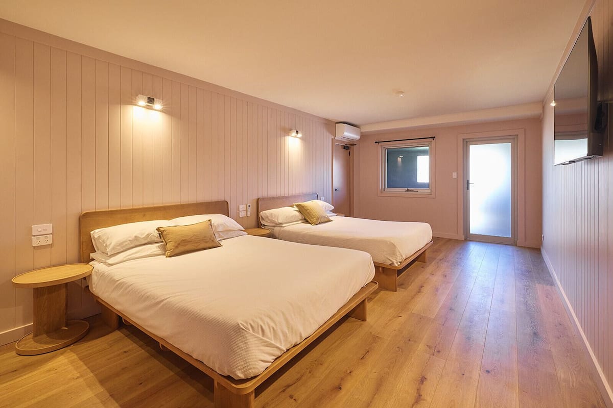 Habitación de hotel con dos camas, suelo de madera y ventana con vistas.