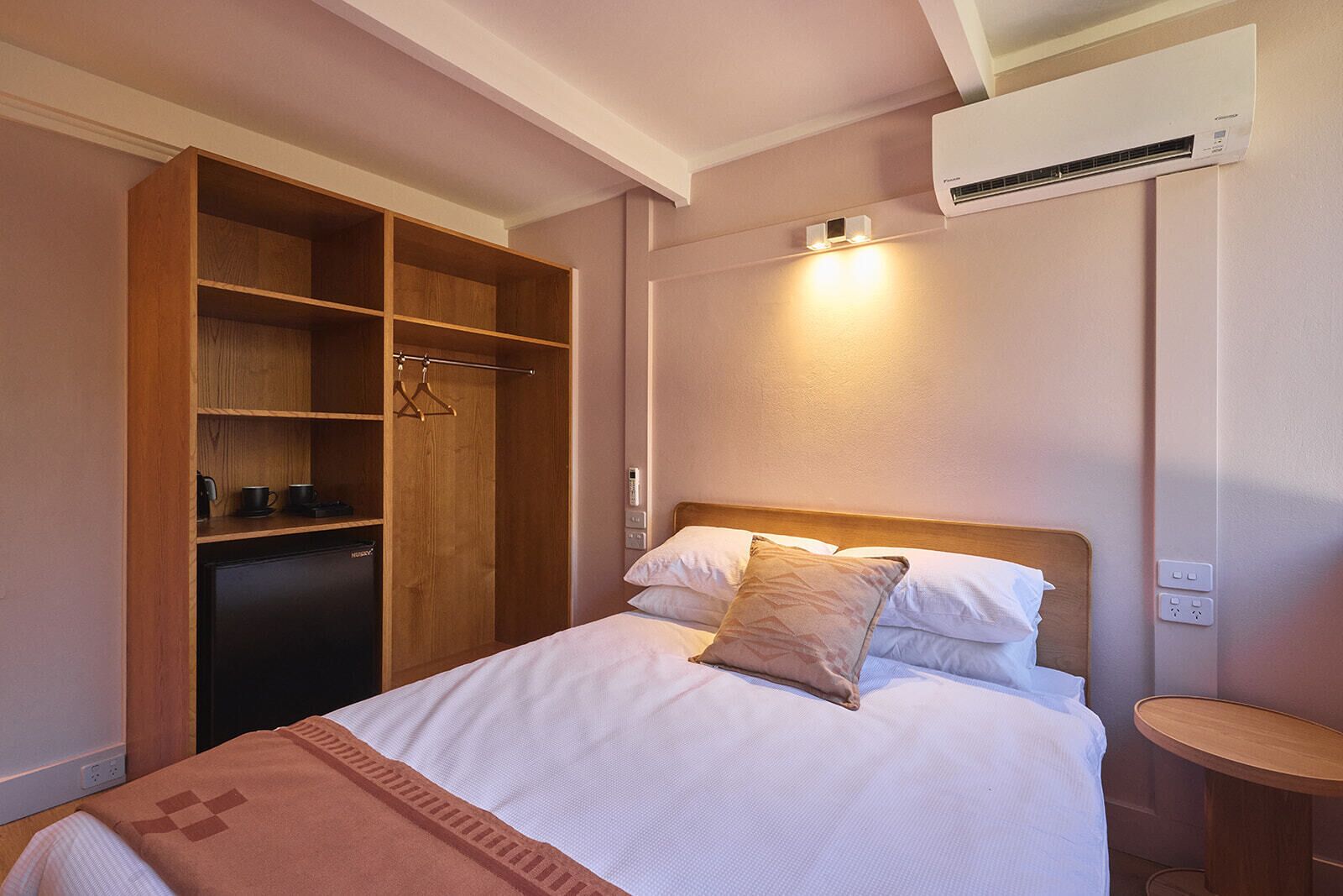 Una habitación de hotel con una cama, un armario, una mesita de noche y un aire acondicionado.