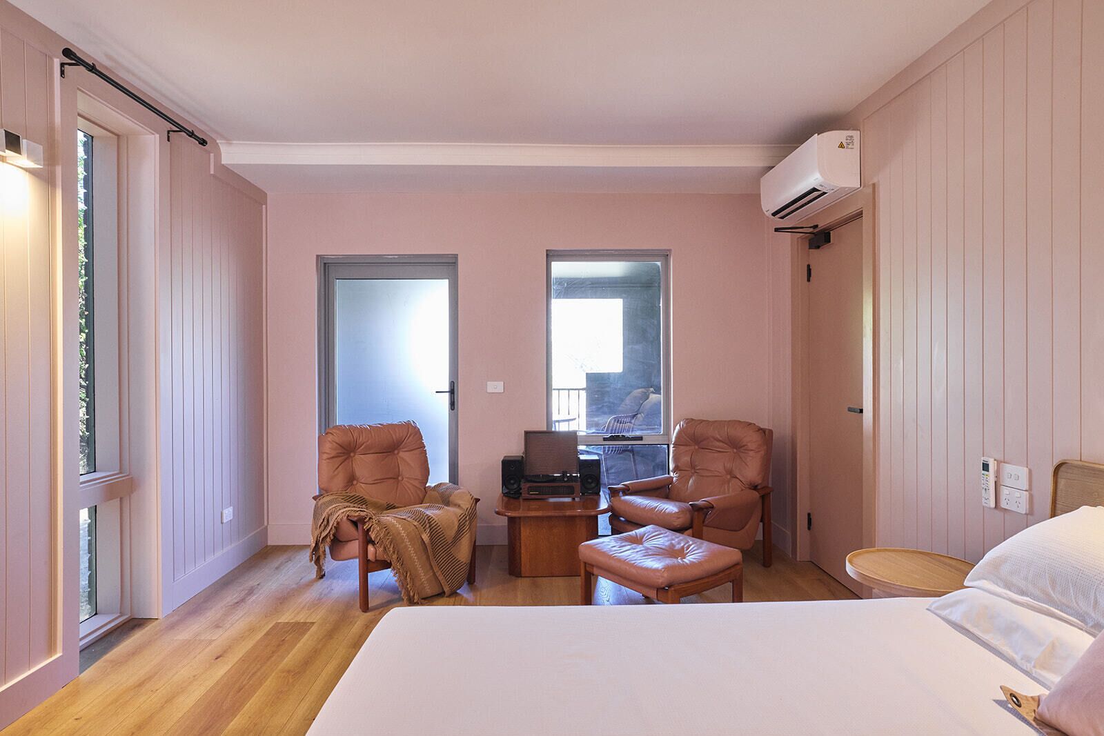 Habitación de hotel con una cama, dos sillones, una mesita con una computadora portátil y un aire acondicionado.