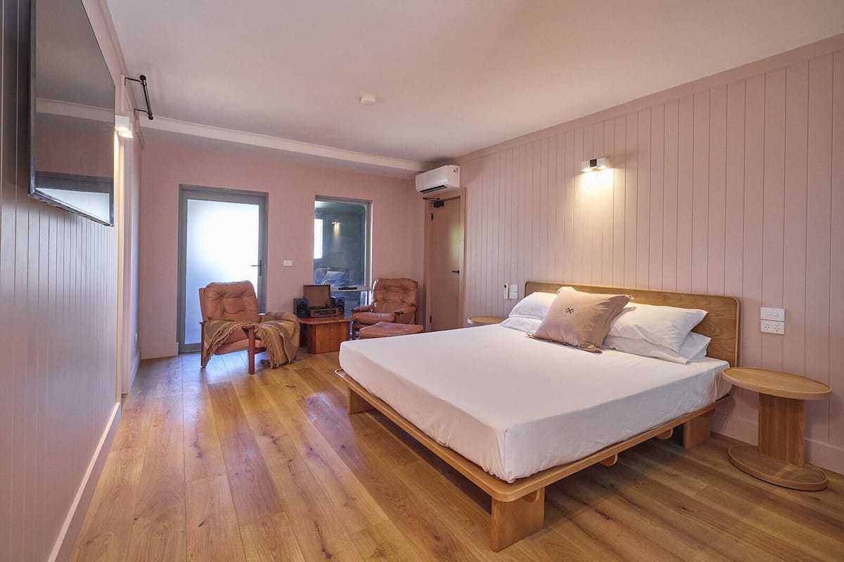 Un dormitorio con una cama grande, dos sillones, una mesita y una mesilla de noche.